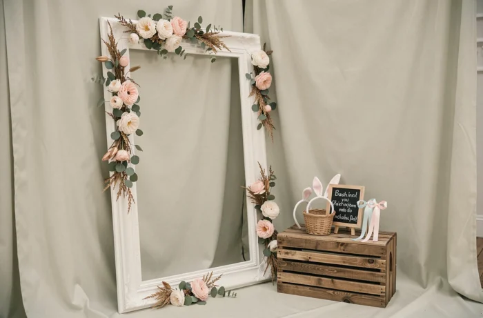 Coin photo de baptême avec cadre géant en bois décoré de fleurs séchées et accessoires simples dans un panier