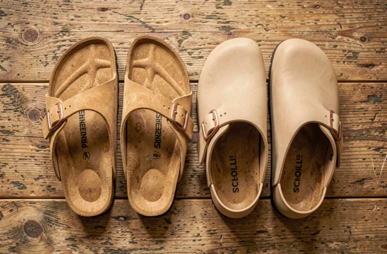 Comparaison entre sandales Birkenstock et sabots Scholl posés côte à côte sur un parquet en chêne rustique